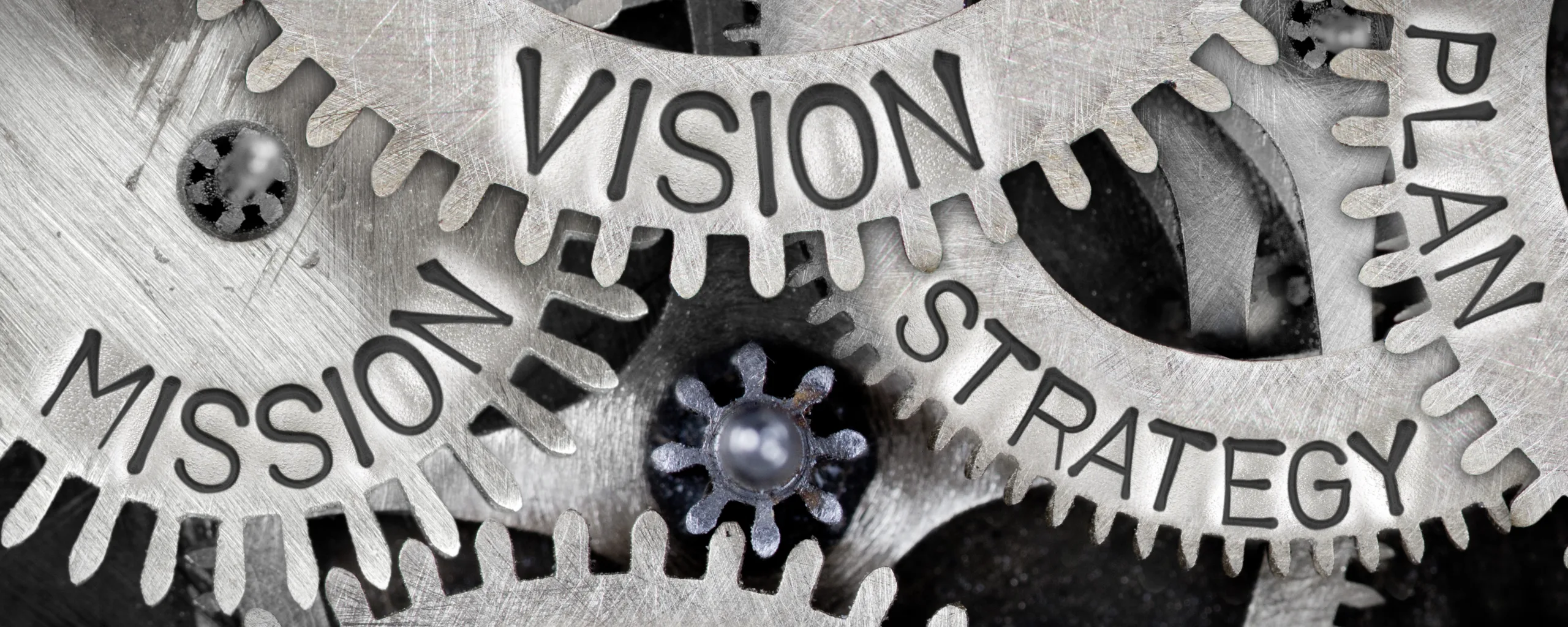 Close-up of interlocking metal gears engraved with the words "Mission," "Vision," "Strategy," and "Plan," symbolizing alignment in business planning and execution.